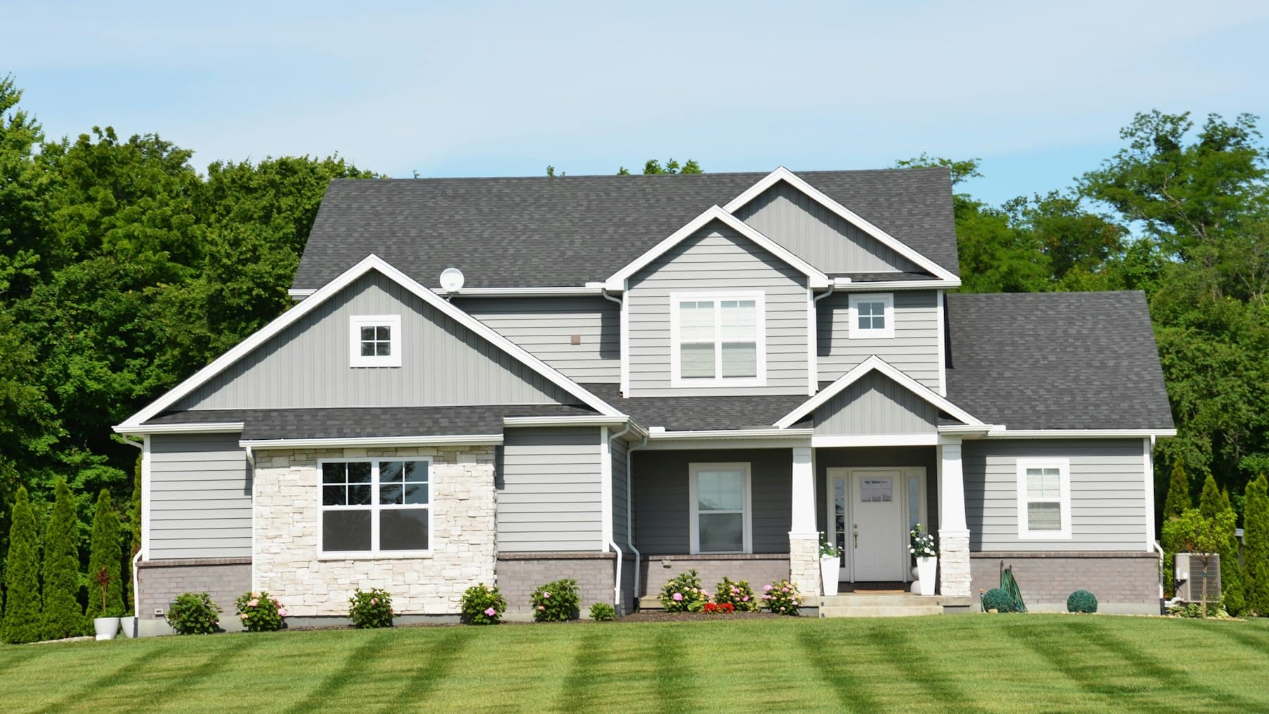 Two-story home with a manicured front lawn, shrubs, and a stone-accented entry