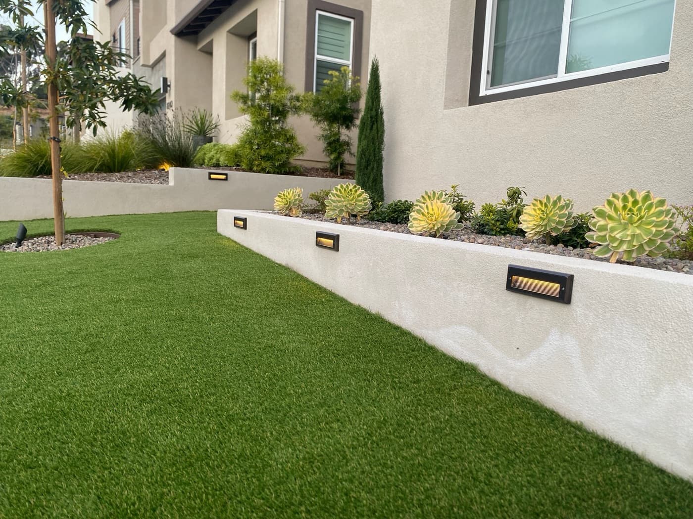 Small turf panel beside a raised planter wall built by Modern Yardz